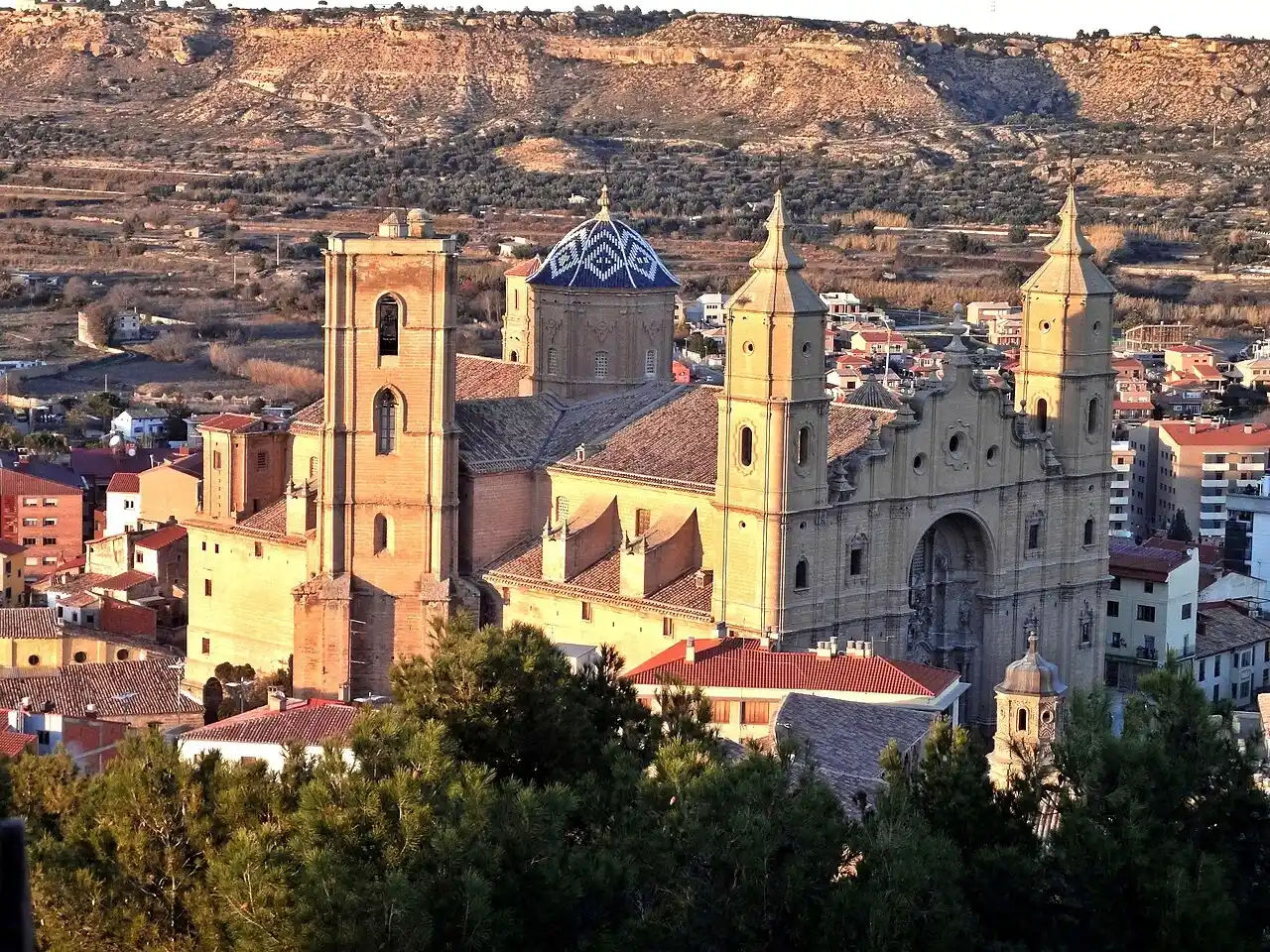 Iglesia con cúpula de azulejos azules entre los tejados de Alcañiz, con campos de cultivo al fondo